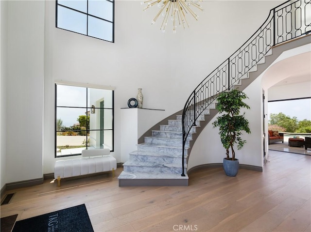 staircase featuring a towering ceiling, hardwood / wood-style flooring, a notable chandelier, and a wealth of natural light