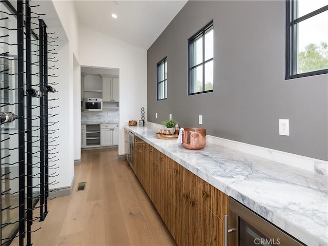 bar featuring stainless steel oven, vaulted ceiling, light hardwood / wood-style flooring, decorative backsplash, and wine cooler