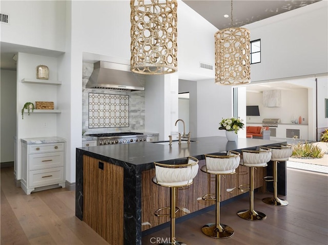 kitchen featuring a high ceiling, wall chimney range hood, backsplash, white cabinetry, and sink