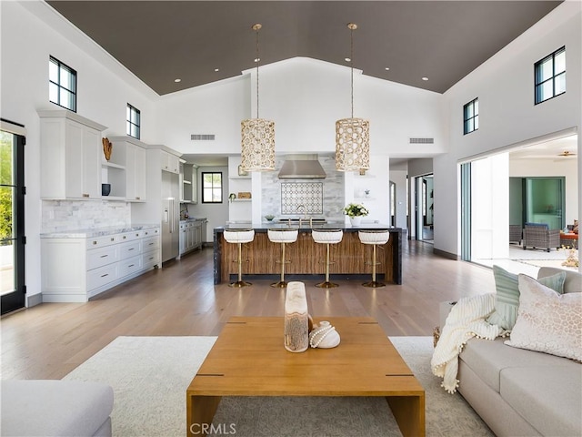 living room featuring a towering ceiling, a chandelier, sink, and light hardwood / wood-style flooring