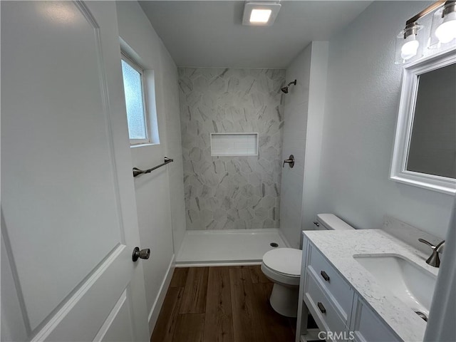 bathroom featuring toilet, tiled shower, vanity, and hardwood / wood-style flooring