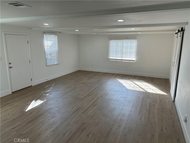 unfurnished room featuring beam ceiling, a barn door, and light hardwood / wood-style flooring