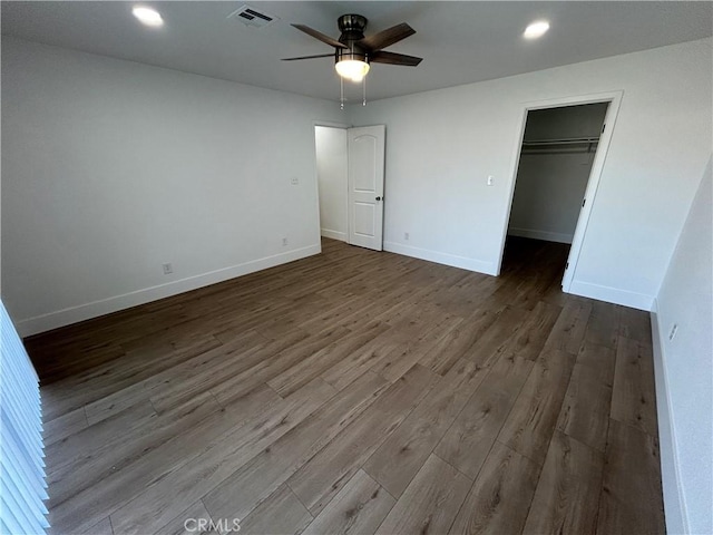 unfurnished bedroom featuring ceiling fan, a walk in closet, a closet, and hardwood / wood-style flooring