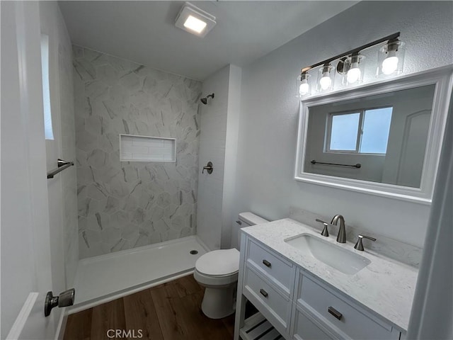 bathroom with a tile shower, vanity, toilet, and hardwood / wood-style flooring