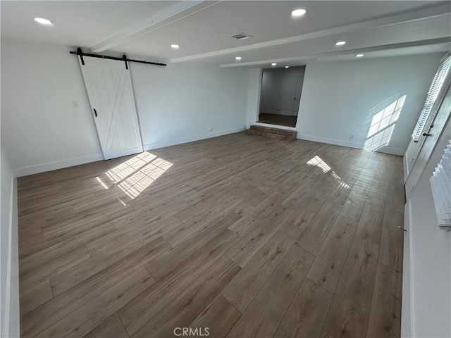 unfurnished room with wood-type flooring, a barn door, and beam ceiling