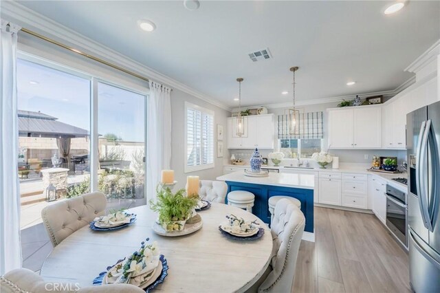 kitchen with stainless steel appliances, decorative light fixtures, white cabinets, a kitchen island, and light hardwood / wood-style flooring