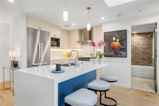 kitchen with hanging light fixtures, sink, light wood-type flooring, wall chimney range hood, and built in appliances