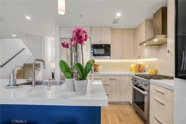 kitchen featuring built in microwave, light brown cabinetry, high end range, and wall chimney range hood