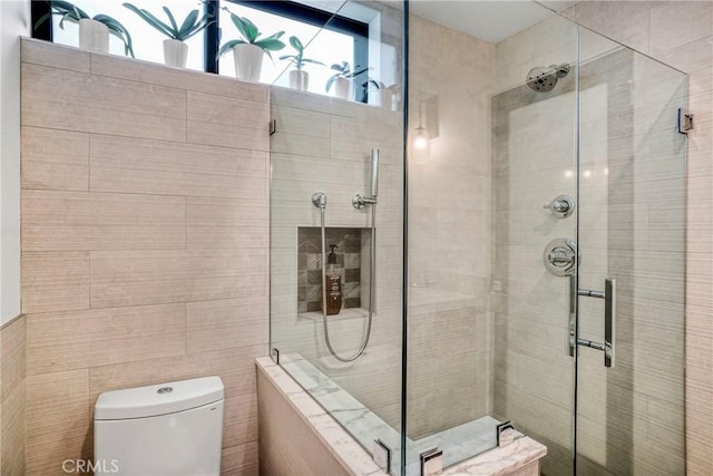 bathroom with toilet, tile walls, and a shower with door