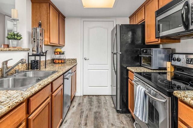 kitchen with sink, light stone countertops, light hardwood / wood-style flooring, and appliances with stainless steel finishes