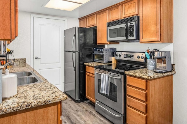 kitchen featuring appliances with stainless steel finishes, light hardwood / wood-style flooring, light stone counters, and sink