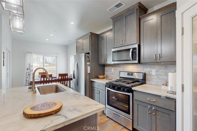 kitchen featuring appliances with stainless steel finishes, decorative light fixtures, tasteful backsplash, sink, and light stone countertops