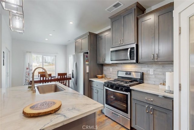 kitchen featuring appliances with stainless steel finishes, pendant lighting, tasteful backsplash, sink, and light stone counters