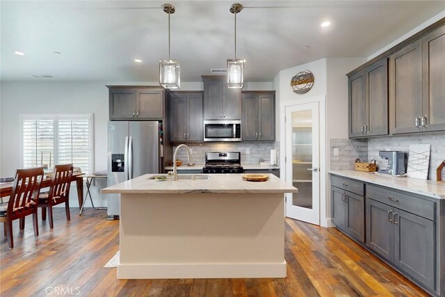 kitchen with stainless steel appliances, an island with sink, sink, and decorative light fixtures