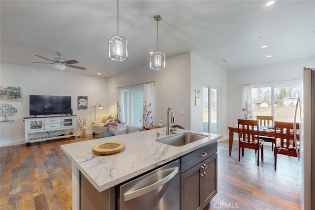 kitchen with pendant lighting, sink, appliances with stainless steel finishes, light stone countertops, and a center island with sink