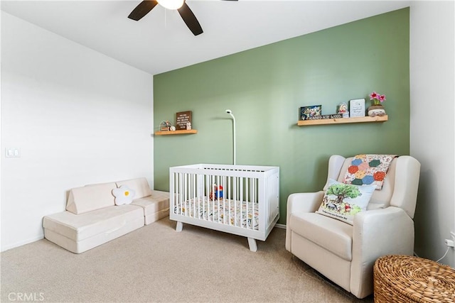 carpeted bedroom featuring a nursery area and ceiling fan