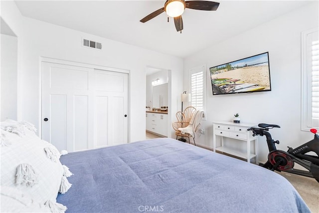 bedroom featuring ceiling fan, light carpet, ensuite bath, and a closet