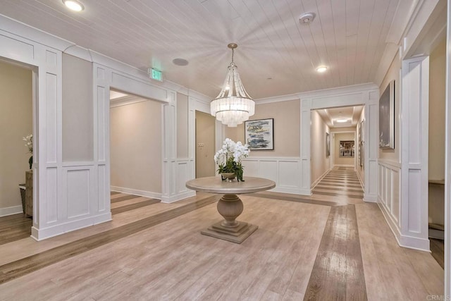 hall with ornamental molding, light hardwood / wood-style floors, and a notable chandelier