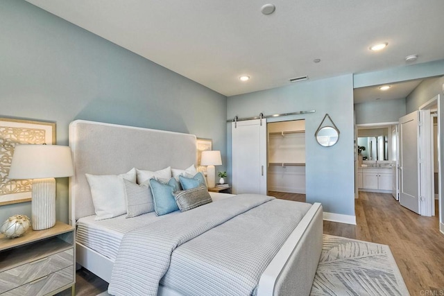 bedroom featuring a spacious closet, connected bathroom, hardwood / wood-style flooring, a closet, and a barn door