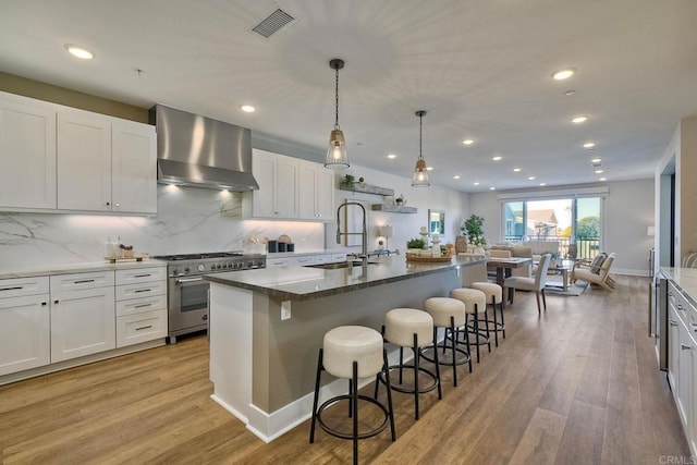 kitchen featuring white cabinets, a kitchen island with sink, sink, extractor fan, and high end stainless steel range