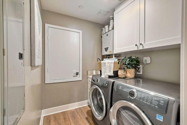 laundry room with tankless water heater, cabinets, washing machine and dryer, and light hardwood / wood-style floors