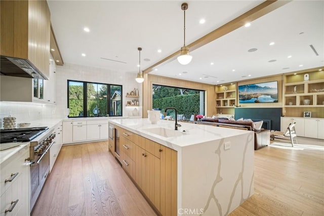 kitchen featuring a spacious island, pendant lighting, light stone countertops, white cabinetry, and sink