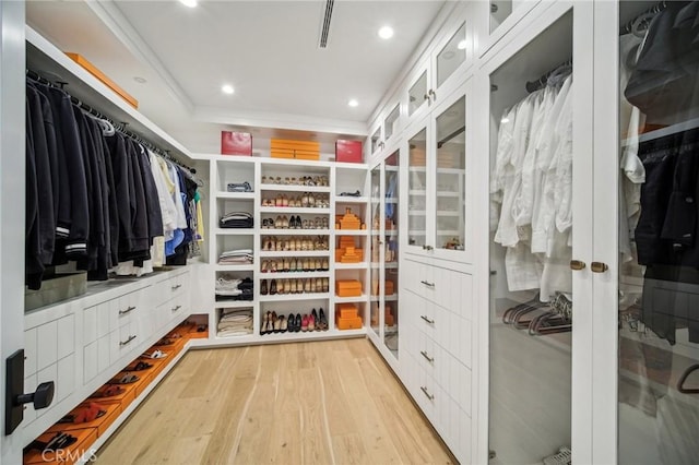 spacious closet with light hardwood / wood-style floors and a tray ceiling