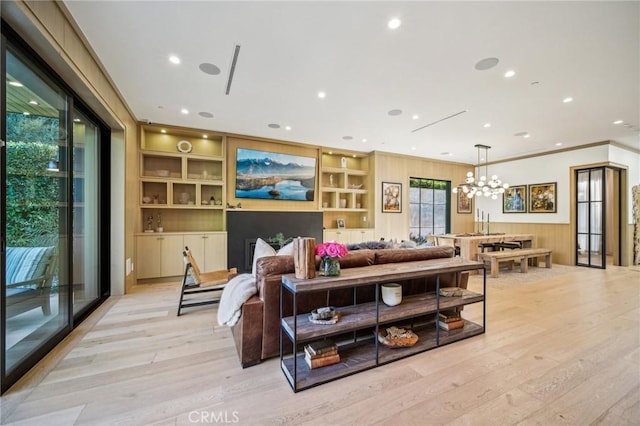 living room featuring built in shelves, a notable chandelier, ornamental molding, wood walls, and light hardwood / wood-style floors