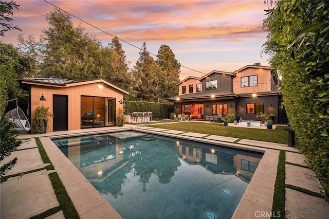 pool at dusk featuring a patio area and an outdoor structure