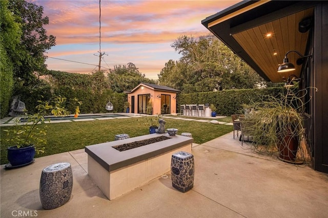 patio terrace at dusk featuring a pool, an outdoor fire pit, an outbuilding, and a yard