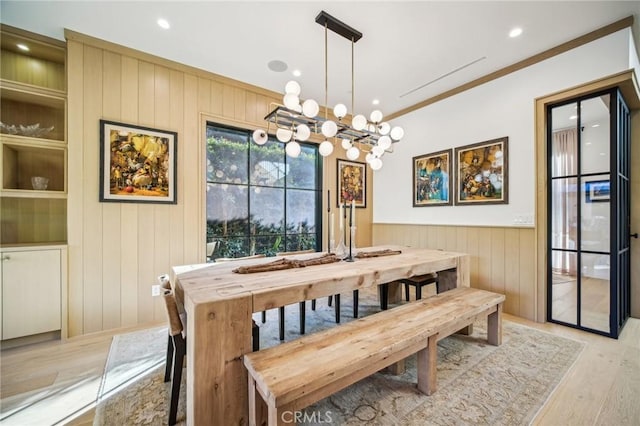 dining area with wood walls, crown molding, and light wood-type flooring