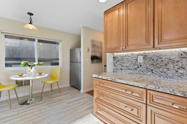 kitchen with decorative backsplash, pendant lighting, light stone counters, and stainless steel refrigerator