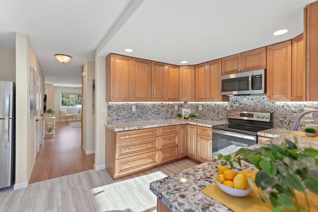 kitchen featuring light wood-type flooring, backsplash, light stone countertops, and stainless steel appliances