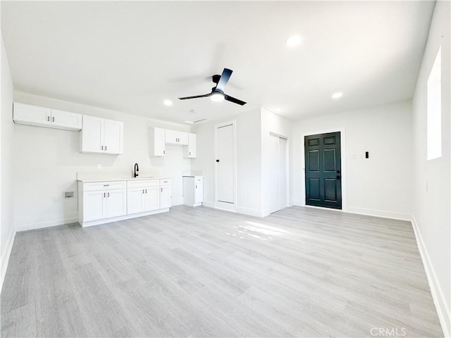 unfurnished living room featuring light hardwood / wood-style floors, ceiling fan, and sink