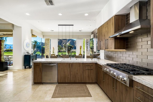 kitchen featuring appliances with stainless steel finishes, kitchen peninsula, sink, wall chimney range hood, and decorative light fixtures