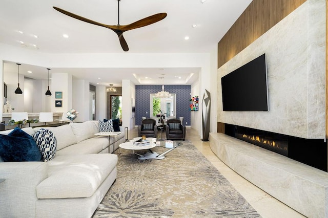 living room featuring a large fireplace, a raised ceiling, and ceiling fan