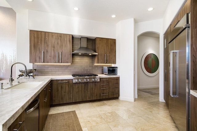 kitchen with appliances with stainless steel finishes, tasteful backsplash, wall chimney range hood, and sink