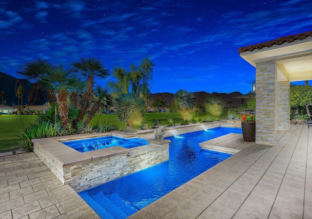 pool at dusk featuring a mountain view, a patio area, pool water feature, and an in ground hot tub