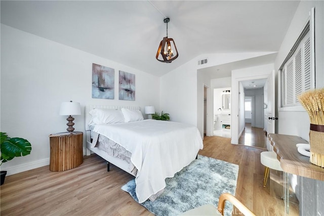 bedroom with connected bathroom, a notable chandelier, hardwood / wood-style floors, and vaulted ceiling