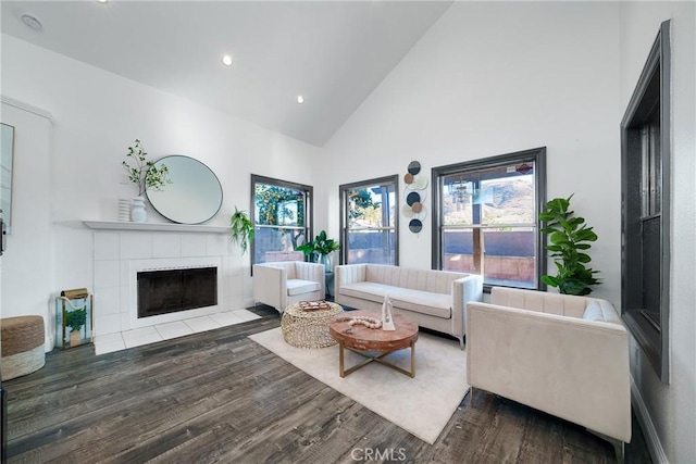 living room with a tiled fireplace, dark wood-type flooring, and high vaulted ceiling