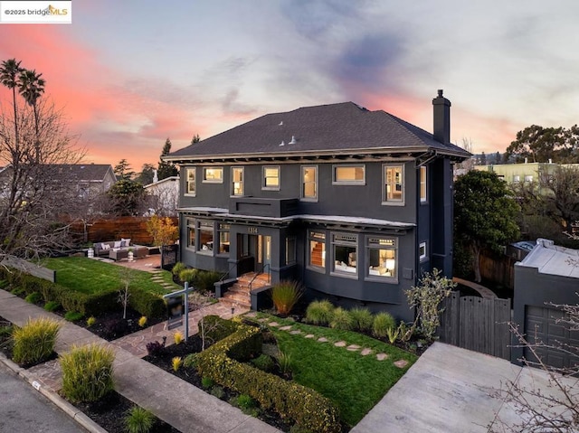 back house at dusk with a patio, a lawn, and outdoor lounge area