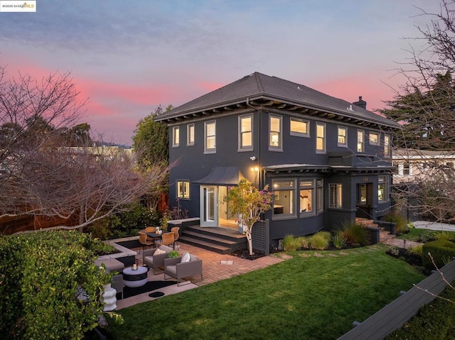 back house at dusk featuring a lawn, a patio area, and an outdoor living space