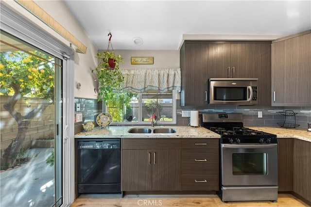 kitchen with light stone counters, appliances with stainless steel finishes, dark brown cabinets, and sink