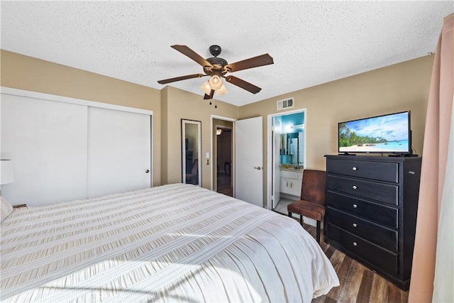 bedroom with a textured ceiling, dark hardwood / wood-style floors, a closet, connected bathroom, and ceiling fan