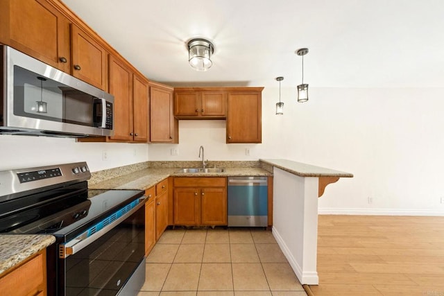 kitchen featuring stainless steel appliances, hanging light fixtures, a sink, light stone countertops, and a peninsula