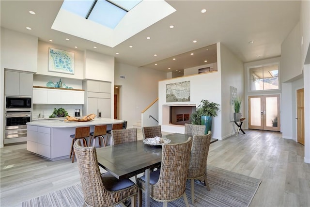 dining area featuring a skylight, a towering ceiling, light hardwood / wood-style flooring, and french doors