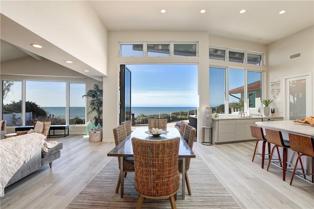 dining space featuring a water view, light hardwood / wood-style flooring, and a high ceiling