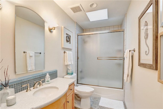 full bathroom featuring combined bath / shower with glass door, a skylight, tasteful backsplash, vanity, and toilet