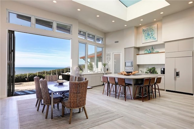 dining room with a water view, a towering ceiling, and light wood-type flooring