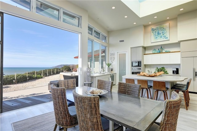 dining area with a water view, light wood-type flooring, and a high ceiling